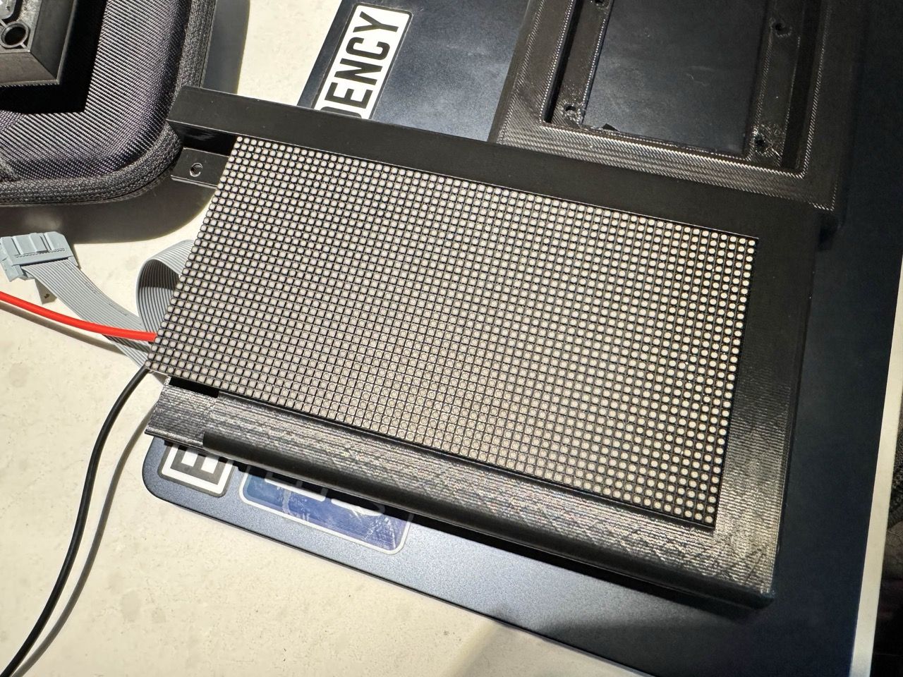 A single LED matrix panel inside one half of a black 3D-printed frame. There are wires sticking out from the back of the display.