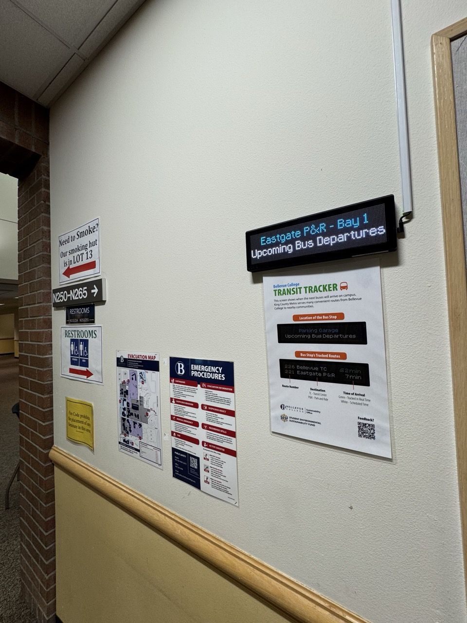 A Transit Tracker mounted on a wall in a hallway with an instructional flyer directly below. It is showing "Eastgate P&R - Bay 1 - Upcoming Bus Departures".